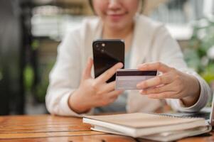 un mujer sentado a un al aire libre espacio, registrando su crédito tarjeta en un compras sitio web. foto