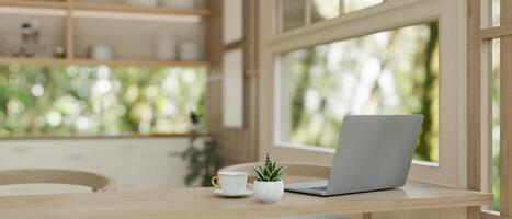 A laptop computer on a wooden dining table near by the window in a neutral contemporary kitchen. photo