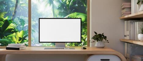 A home office features a computer on a desk against the window with a view of a tropical forest. photo