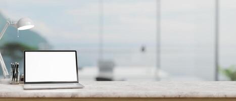 A laptop mockup, a table lamp, and stationery on a white marble table in a modern spacious office. photo