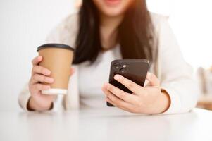 A young Asian woman enjoying a coffee in a cafe while reading messages on her smartphone. photo