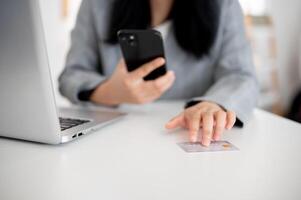 un mujer de negocios sentado a un mesa con su teléfono inteligente y un crédito tarjeta, utilizando un móvil bancario aplicación foto