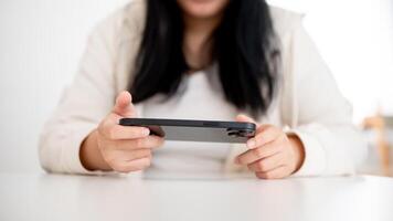 un joven asiático mujer es utilizando su teléfono inteligente, acecho un o jugando un móvil juego adentro. foto