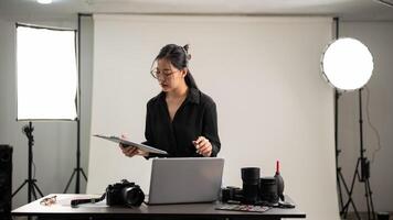 Female photographer is focusing on checking photoshoot details on a clipboard, working in her studio photo