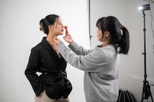 A female model is having makeup applied by a makeup artist, preparing for a photoshoot in the studio photo