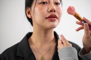 A female model is having makeup applied by a makeup artist, preparing for a photoshoot in the studio photo