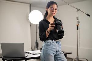 profesional asiático hembra fotógrafo es enfoque en ajustando su dslr cámara, trabajando en un estudio foto