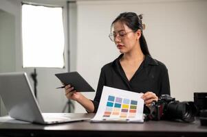 profesional asiático hembra fotógrafo es mirando a un color inspector, trabajando en un Sesión de fotos estudio