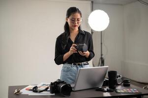 profesional asiático hembra fotógrafo es preparando su cámara para un Sesión de fotos, trabajando en un estudio foto