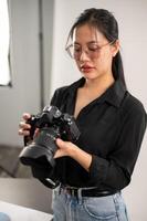 A confident, experienced Asian female photographer is adjusting her DSLR camera, preparing photoshoot equipment, and working in the studio. photo