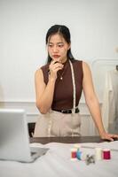 A professional, confident Asian female fashion designer is working in her studio. photo