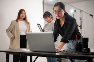 A confident female photographer checking images on her laptop, working with her team in the studio. photo