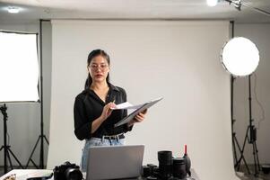 Female photographer is focusing on checking photoshoot details on a clipboard, working in her studio photo