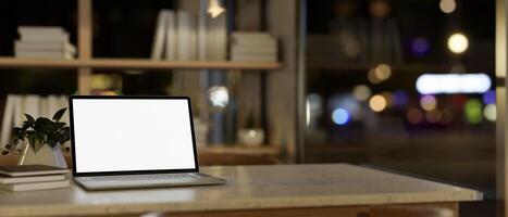 A white-screen laptop computer mockup on a desk in a modern home office at night. photo