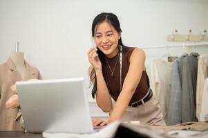 A professional, busy female tailor is talking on the phone with while working in her studio. photo