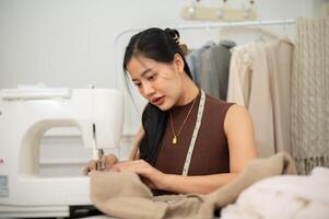 A professional Asian female tailor or fashion designer is sewing a dress with a sewing machine. photo