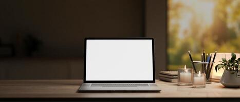 A white-screen laptop computer mockup and decor on a hardwood desk in a modern dark home office. photo