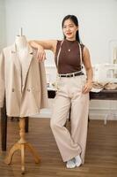 A confident Asian female fashion designer is standing in her atelier studio with a tailor dummy. photo