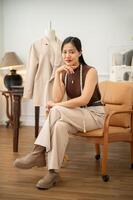 An attractive Asian female fashion designer is sitting on an armchair in her atelier studio. photo