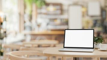 A white-screen laptop computer mockup on a wooden table in a contemporary cosy coffee shop. photo