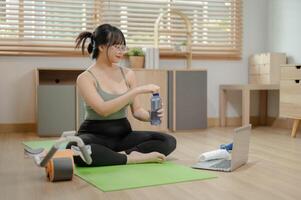A healthy, fit young Asian woman in sportswear is taking a break after exercise, sipping water. photo