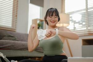 un saludable, contento joven asiático mujer comprobación su quemado calorías, sentado en un yoga estera. foto