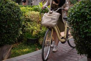A cropped shot of a woman in a cute dress pushing her bicycle on a footpath in a city park. photo