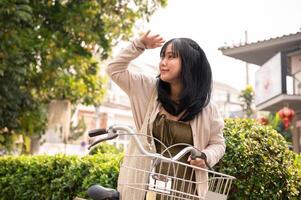 A happy young Asian woman exploring the city with her bicycle, finding a grocery store. photo