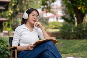 A calm Asian woman is keeping her eyes closed, listening to music while sitting in her backyard. photo