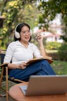 Happy Asian woman is listening to music, working or writing her diary while sitting in her backyard. photo