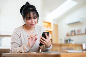 A happy Asian woman is using her smartphone while sitting in a cosy coffee shop. photo