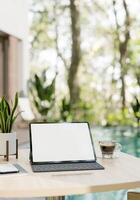 A digital tablet mockup, a wireless keyboard, a coffee cup, and decor on a table by the pool. photo