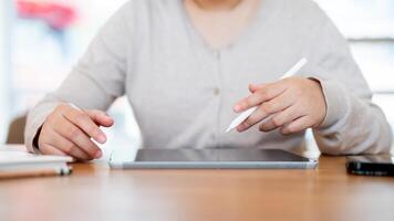 A cropped shot of a woman working on her digital tablet at a table indoors or in a minimalist cafe. photo