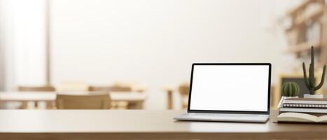 A wooden table features a laptop mockup in a cosy neutral coffee shop or library co-working space. photo