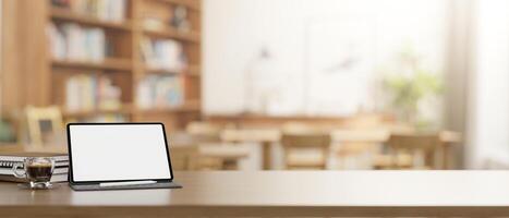 A wooden table features a digital tablet mockup over a blurred background of a school library. photo