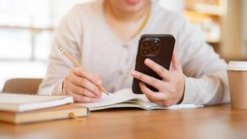 A cropped shot of a woman using her phone while working on her tasks at a table in a coffee shop. photo