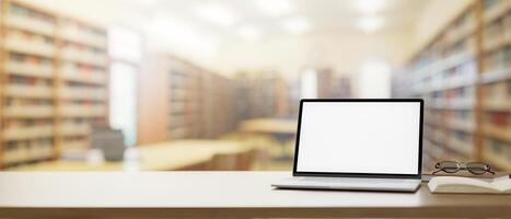 A wooden table features a laptop computer mockup over a blurred background of a school library. photo