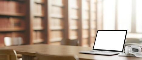 A white-screen laptop computer mockup on a wooden table in a library. photo