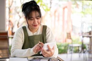 A positive Asian female small business owner using a calculator, calculating her shop revenue. photo