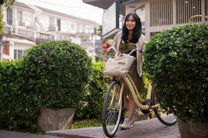 A happy, beautiful young Asian woman is pushing her bicycle on a footpath in the city. photo