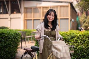 A smiling young Asian woman in a cute dress with her bicycle in the city on a sunny day. photo