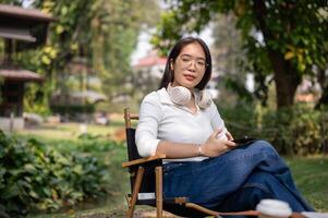 An Asian woman relaxing in her backyard, sitting on a camping chair with a smartphone in her hand. photo