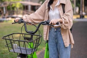 A cropped shot of a female college student is pushing her bicycle in a green park. photo