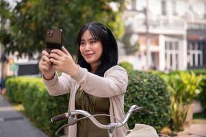 un mujer es tomando un imagen de el ciudad con su teléfono inteligente mientras explorador eso con su bicicleta. foto