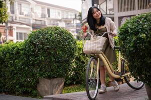 A happy, beautiful young Asian woman is pushing her bicycle on a footpath in the city. photo