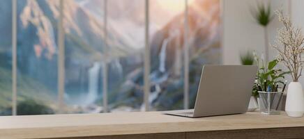 A laptop on a table in a modern office with an amazing large window with a snowy mountains view. photo