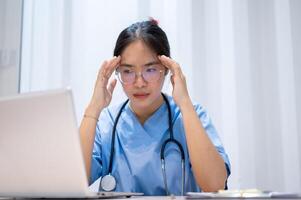 A stressed, overworked, and tired Asian female doctor is reading her medical cases on a laptop. photo