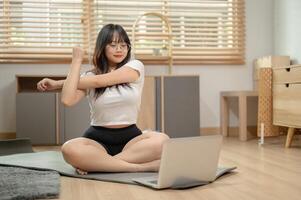 A fit woman is stretching her body on a yoga mat while watching an online yoga tutorial . photo