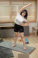 un fuerte asiático mujer en ropa de deporte es extensión su núcleo músculos y brazos en un yoga estera. foto