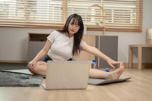 un ajuste asiático mujer en ropa de deporte es haciendo yoga a hogar, siguiendo el yoga tutorial en línea. foto